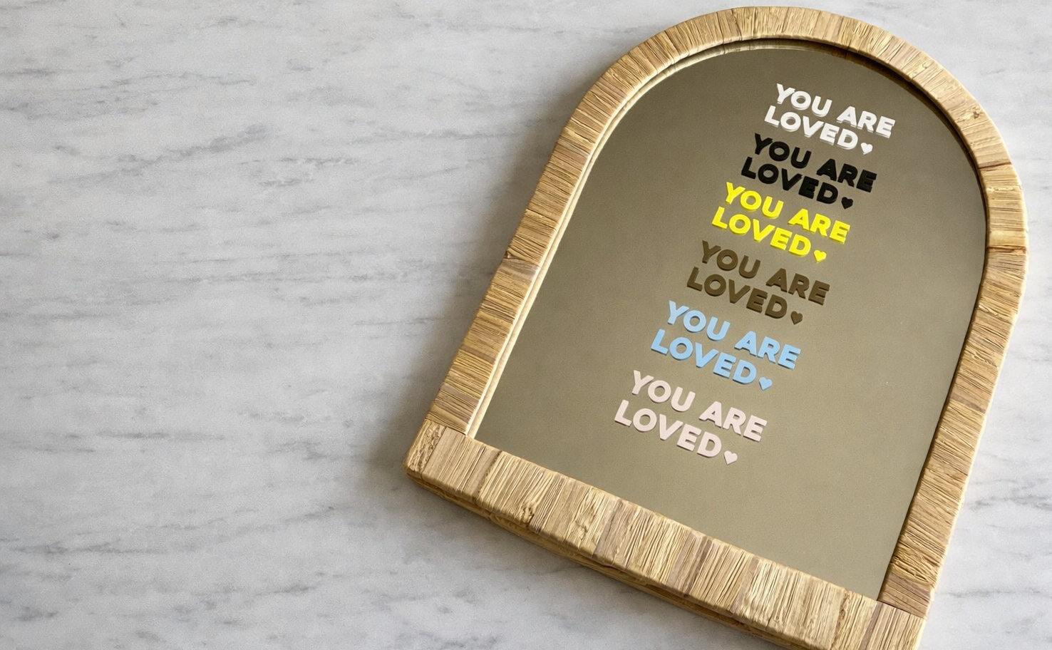Decorative mirror with 'You are loved' text shown in the 6 colours available for affirmation stickers on a marble table top