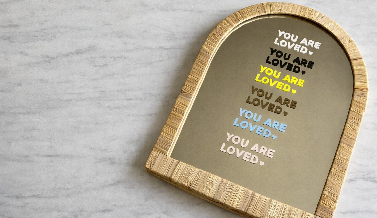 Decorative mirror with 'You are loved' text shown in the 6 colours available for affirmation stickers on a marble table top